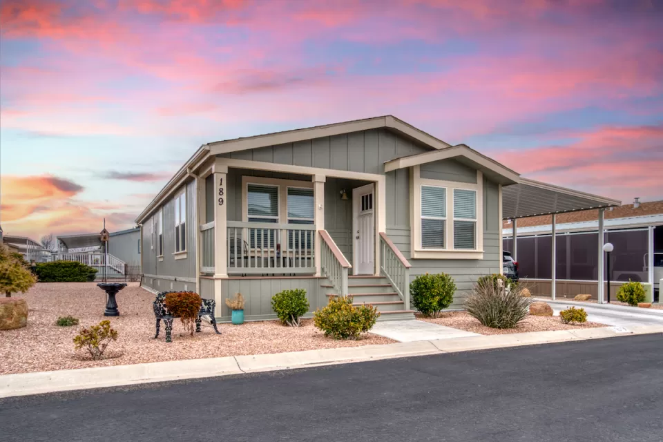 Front of pale green manufactured home with carport and desert sunset in background.